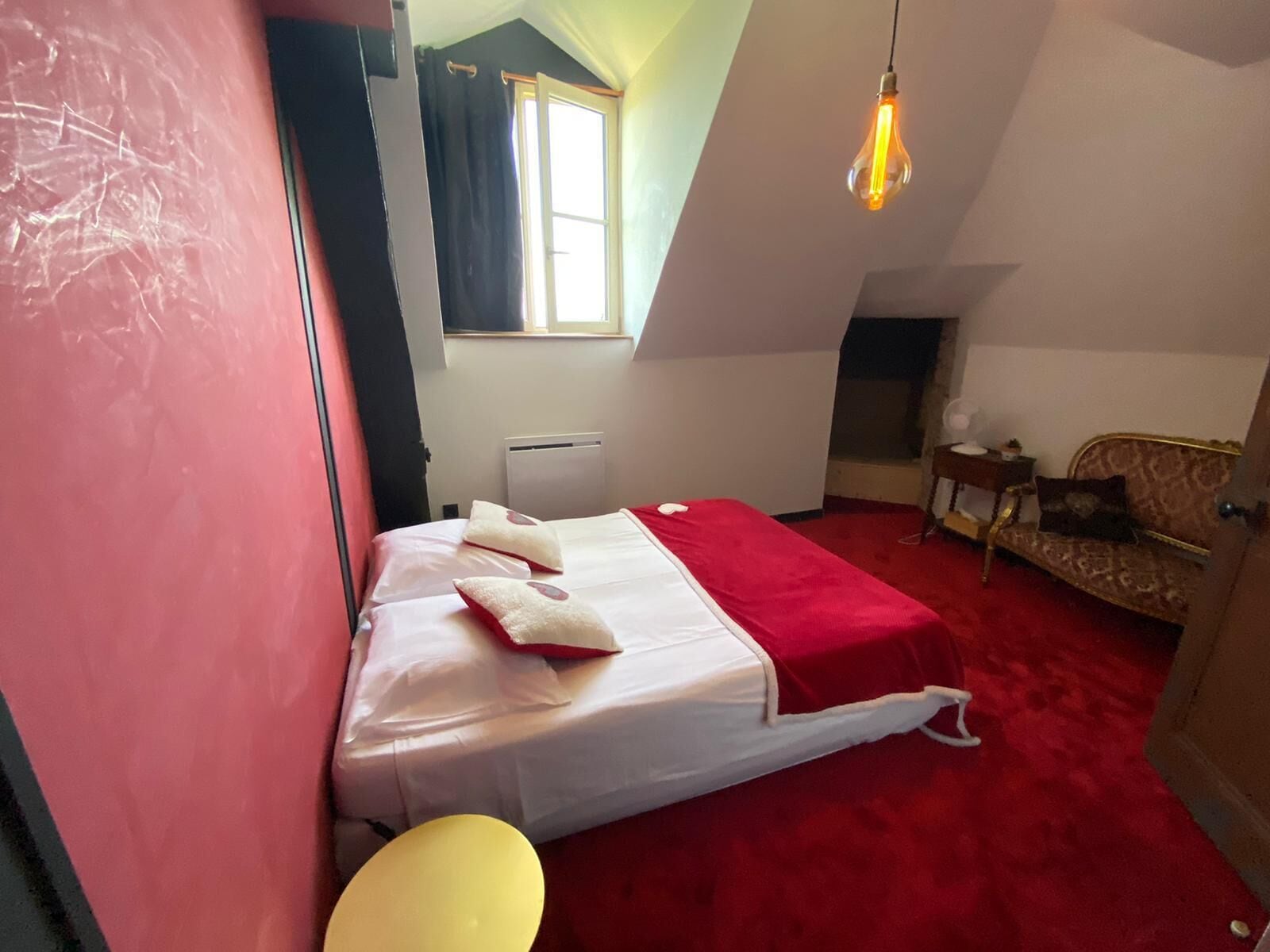 Une petite pièce agréable et chaleureuse, avec un lit, un canapé, une fenêtre et un luminaire suspendu.