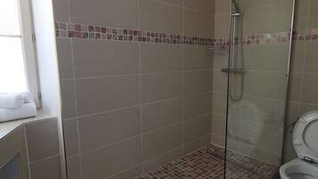 A bathroom with a shower, toilet, and a window.