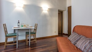 A room with a dining table, two chairs, a sofa, and a door leading to another room. - Borgo Pinti Apartment (Florence)