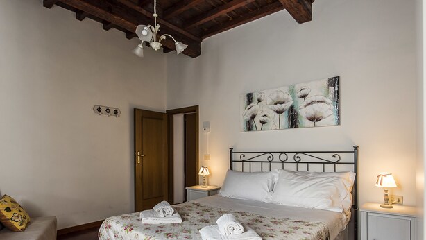 A bedroom with a bed, two bedside tables with lamps, a wooden door, and a floral bedspread. - Borgo Pinti Apartment (Florence)
