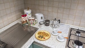A kitchen with a stainless steel sink, a stove, a coffee maker, a kettle, a roll of paper towels, a bag of coffee, and a plate with waffles. - Borgo Pinti Apartment (Florence)
