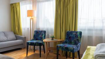 Une chambre d’hôtel avec un canapé, deux fauteuils à motifs, une petite table avec une lampe et un lit.