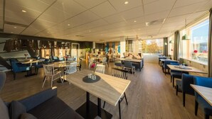 A modern restaurant with a mix of seating options, including tables and booths, and a large window providing a view of the outdoors. - Thon Hotel Sortland (Sortland)