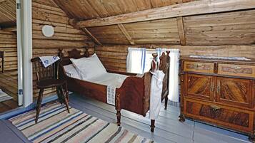 Une pièce de cabane en bois comprenant un lit, une chaise, une commode et une fenêtre avec des rideaux.