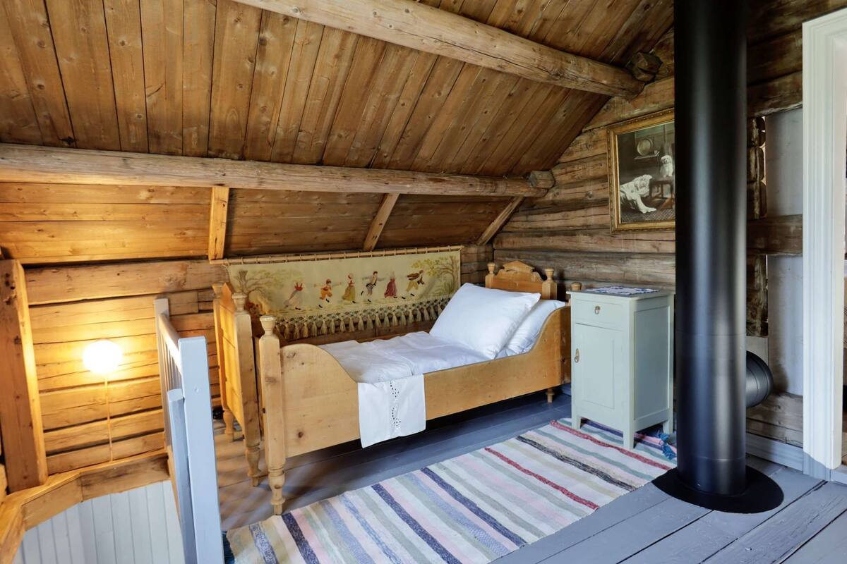 A wooden cabin room with a bed, a small cabinet, and a fireplace.