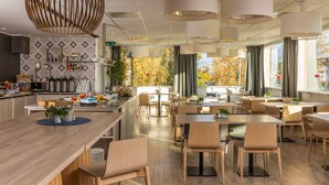 A modern restaurant with a long counter, multiple tables, and hanging pendant lights.