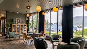 A modern interior with a wooden floor, green upholstered chairs, a round table, and a bookshelf.
