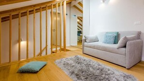 Een moderne woonkamer met een grijze bank, een zacht tapijt en houten balken in het plafond.
