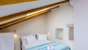 Een slaapkamer met een schuine kap, een bed met witte beddengoed, een blauw accent op de sprei, en een handdoek op het bed.