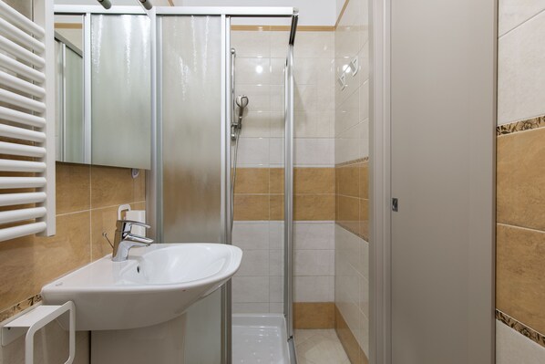 Un baño con ducha envuelta en vidrio, un lavamanos blanco y un espejo.