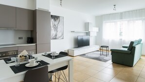 A modern living room with a sofa, a TV, and a dining area with a table and chairs. - Prestige Du Lac Apartments (Lugano)
