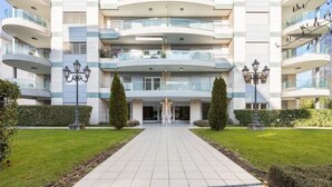 A modern multi-story building with a central entrance, surrounded by well-maintained lawns and decorative street lamps. - Prestige Du Lac Apartments (Lugano)