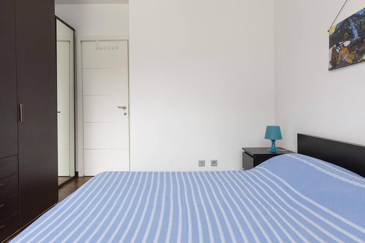 Una camera da letto con un letto, un comodino, una lampada e una porta.