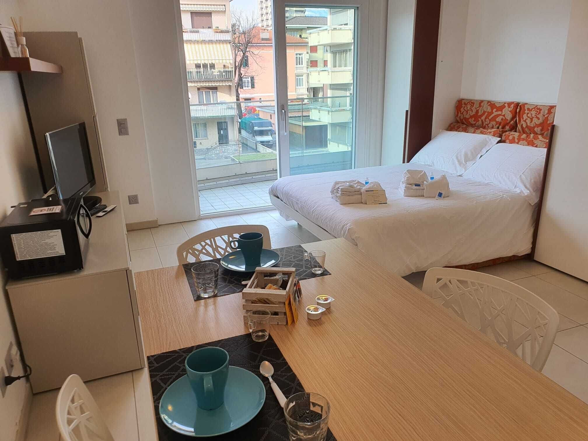 Habitación de hotel con cama, escritorio, televisión y vista al balcón exterior.