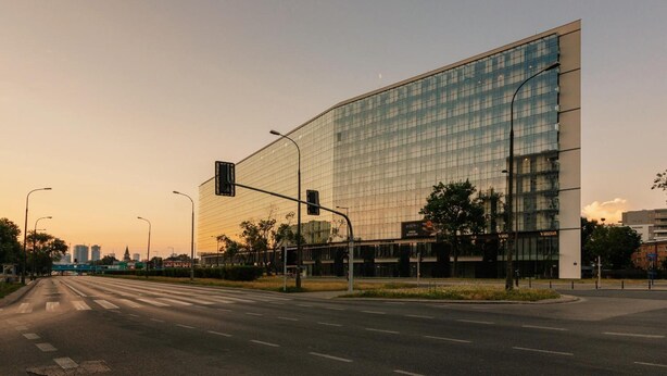 Um edifício moderno com fachada de vidro, situado no cruzamento de ruas.