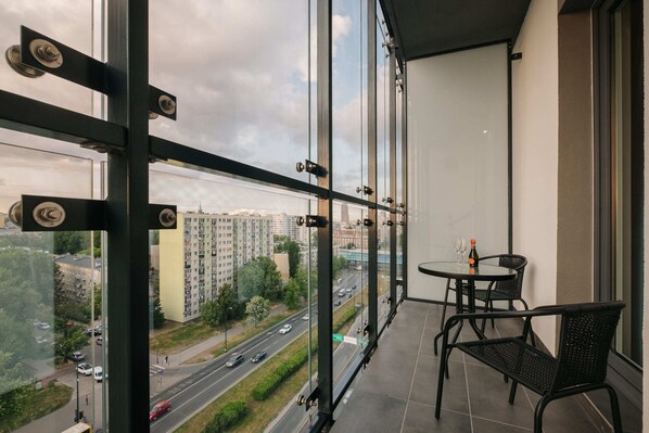 A balcony with a view of a cityscape, a round table with chairs, and a bottle of champagne.