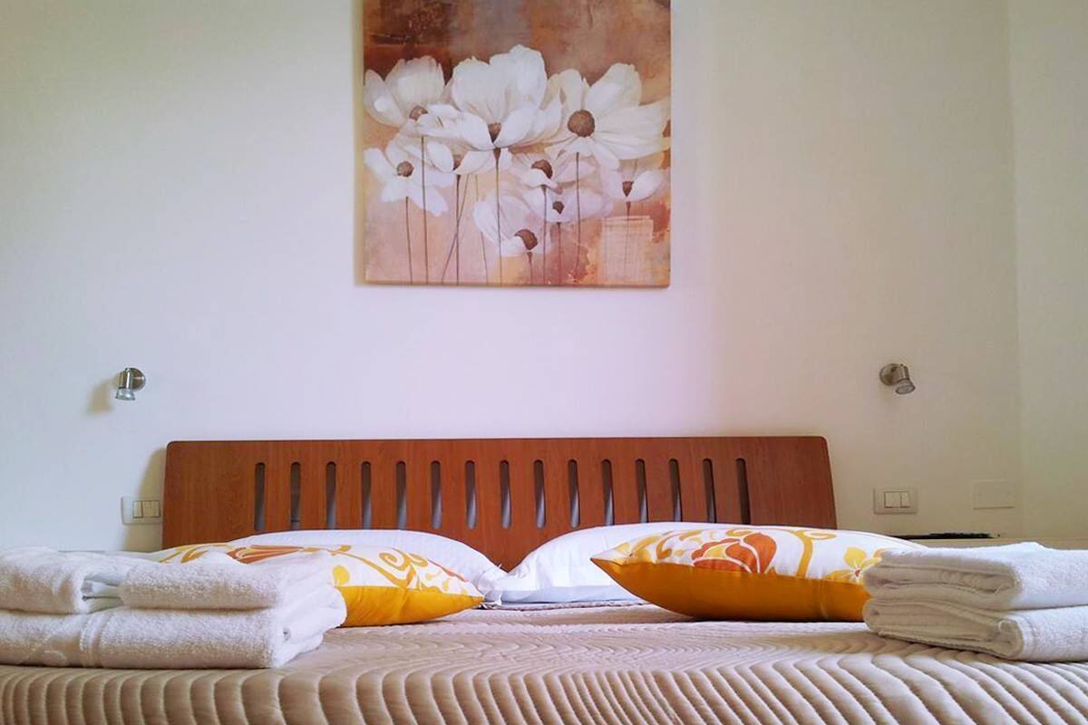 A neatly made bed with a wooden headboard, two pillows with a floral pattern, and a stack of folded towels.