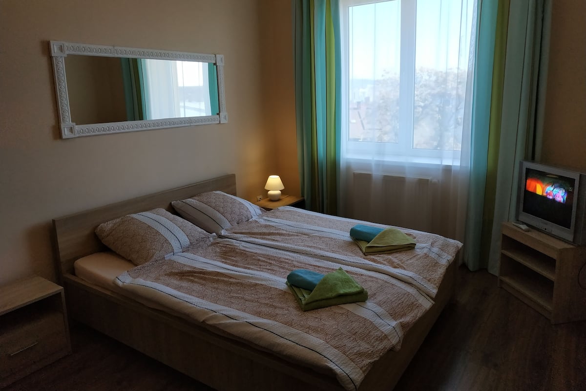 A hotel room with a bed, a TV, a lamp, and a window with curtains.