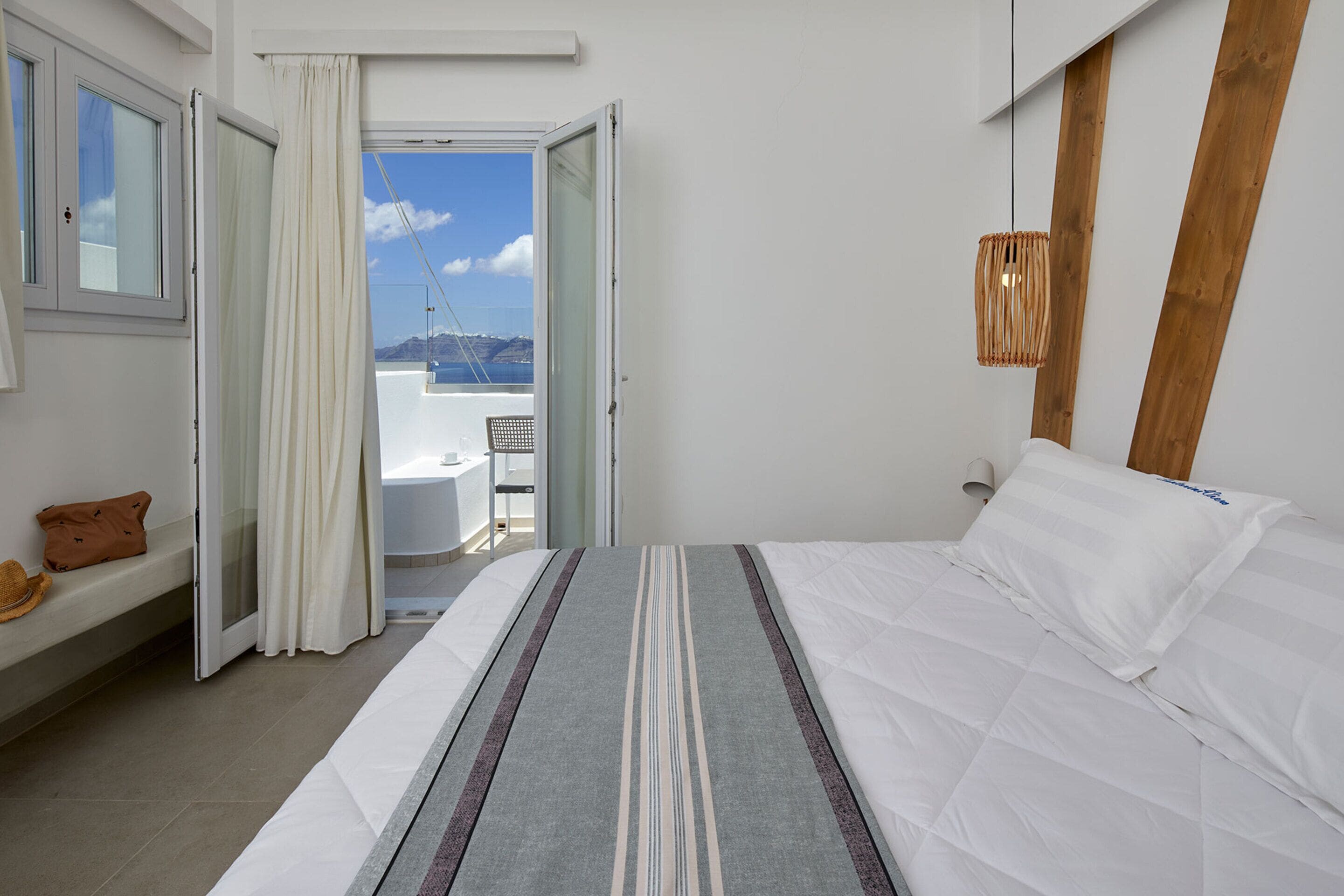 Una camera da letto con un letto, una panca con un cappello, vista sul mare e una trave in legno al muro.