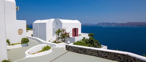 A white building with a stone wall and a view of the sea.