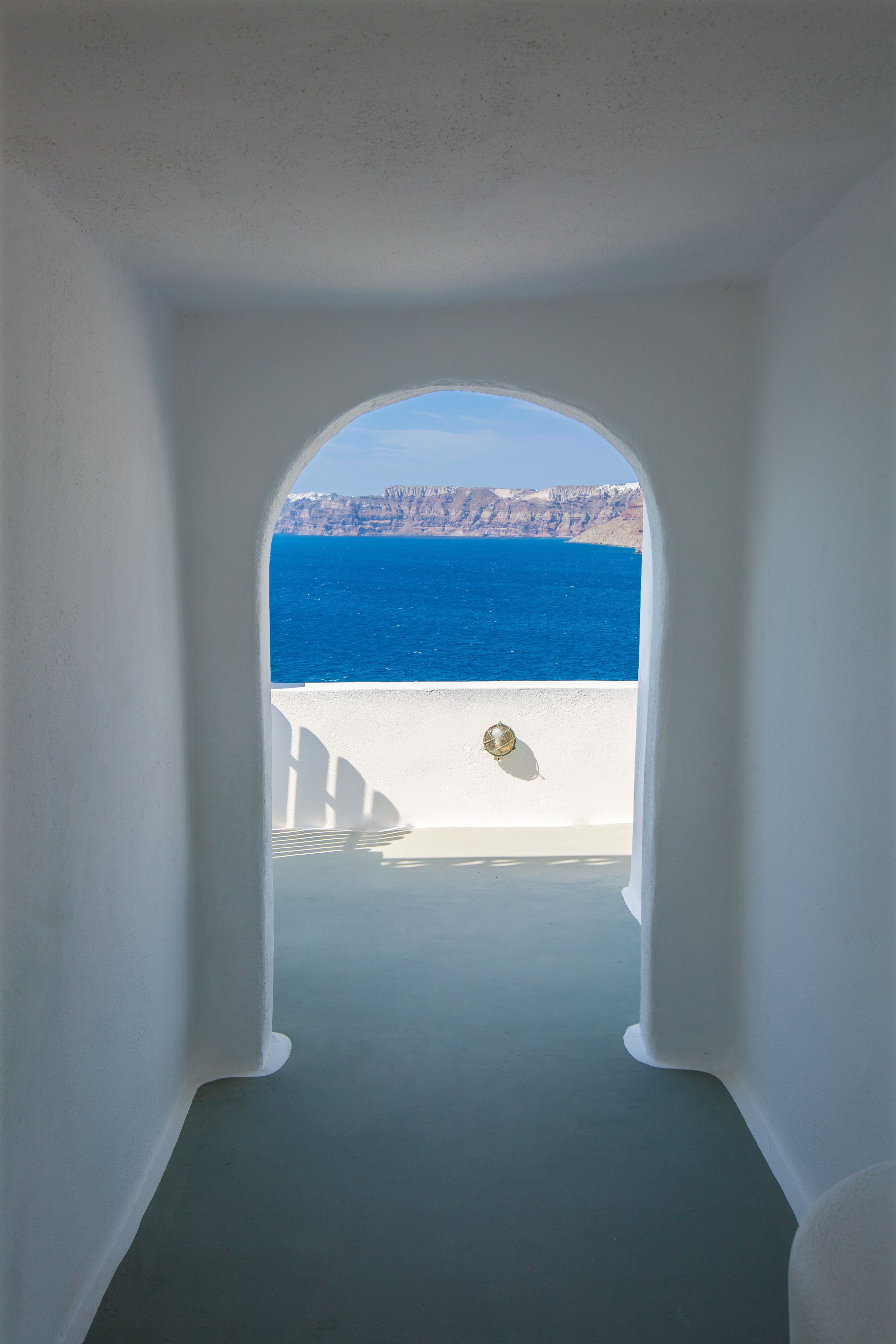 An arched doorway leading to a balcony with a view of the sea and cliffs.