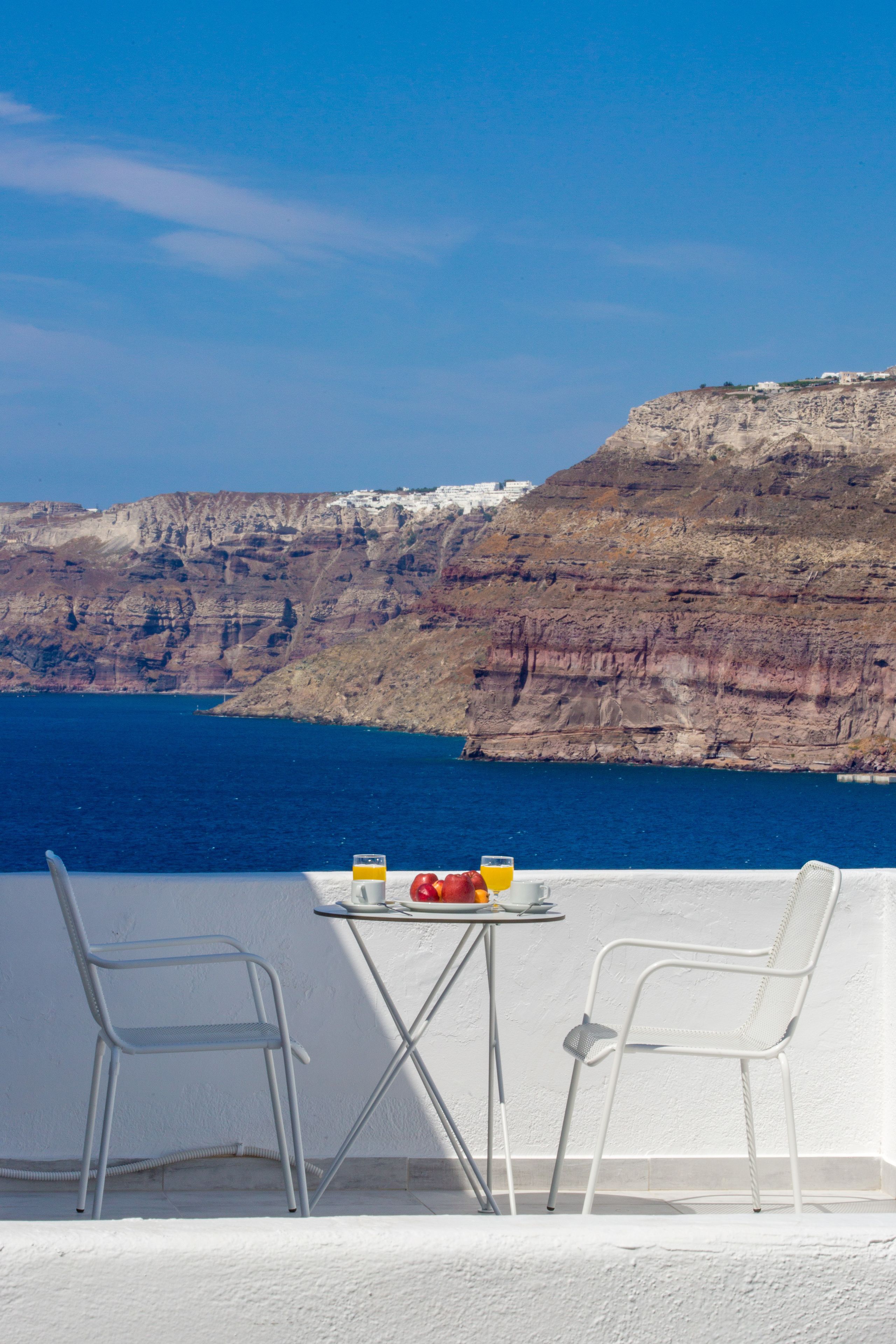 A balcony with two white chairs and a small table, overlooking a coastal cliff and the sea.