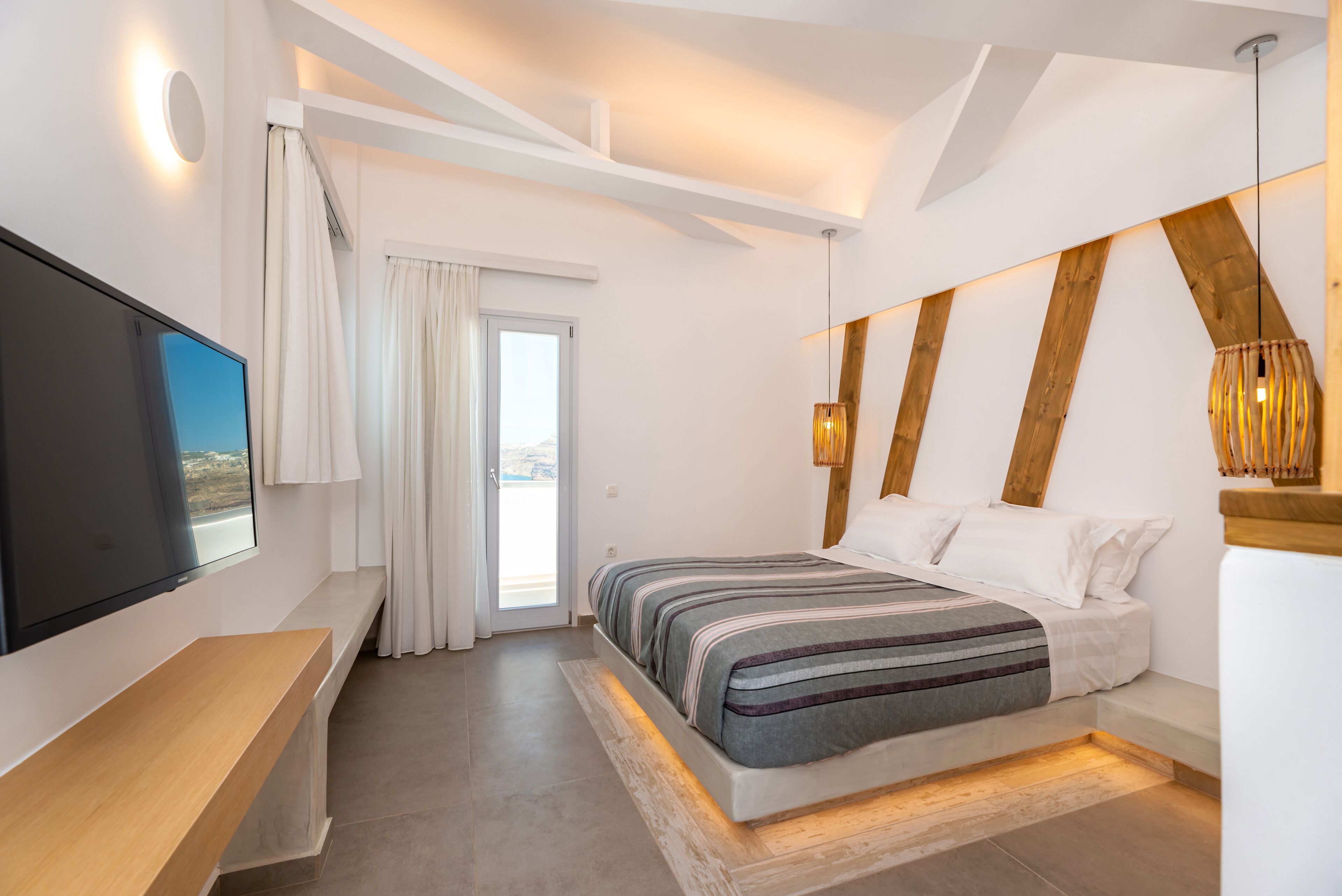 A modern bedroom with a large bed, a TV mounted on the wall, and a wooden bench.