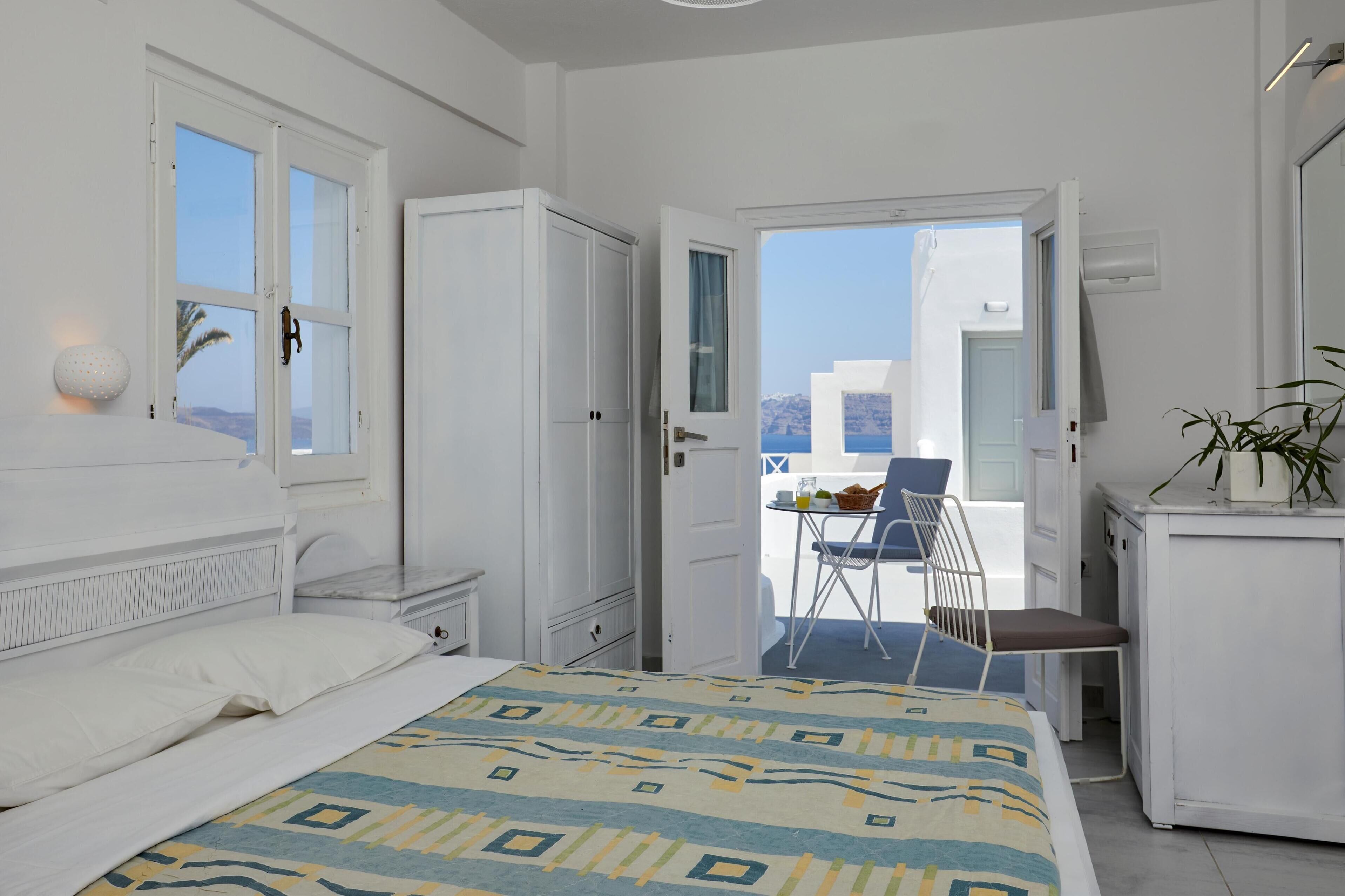 A bedroom with a bed, a wardrobe, a desk with a chair, and a balcony with a table and chairs.