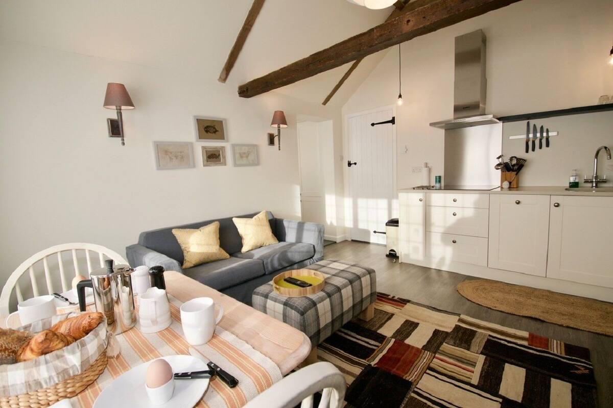 A cozy living room with a sofa, a dining table with breakfast items, and a kitchen with white cabinets and a hanging knife rack.