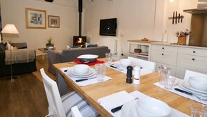 A dining area with a wooden table set for four, white chairs, and a kitchen in the background. - Fazeboons Barn (Woodbridge)