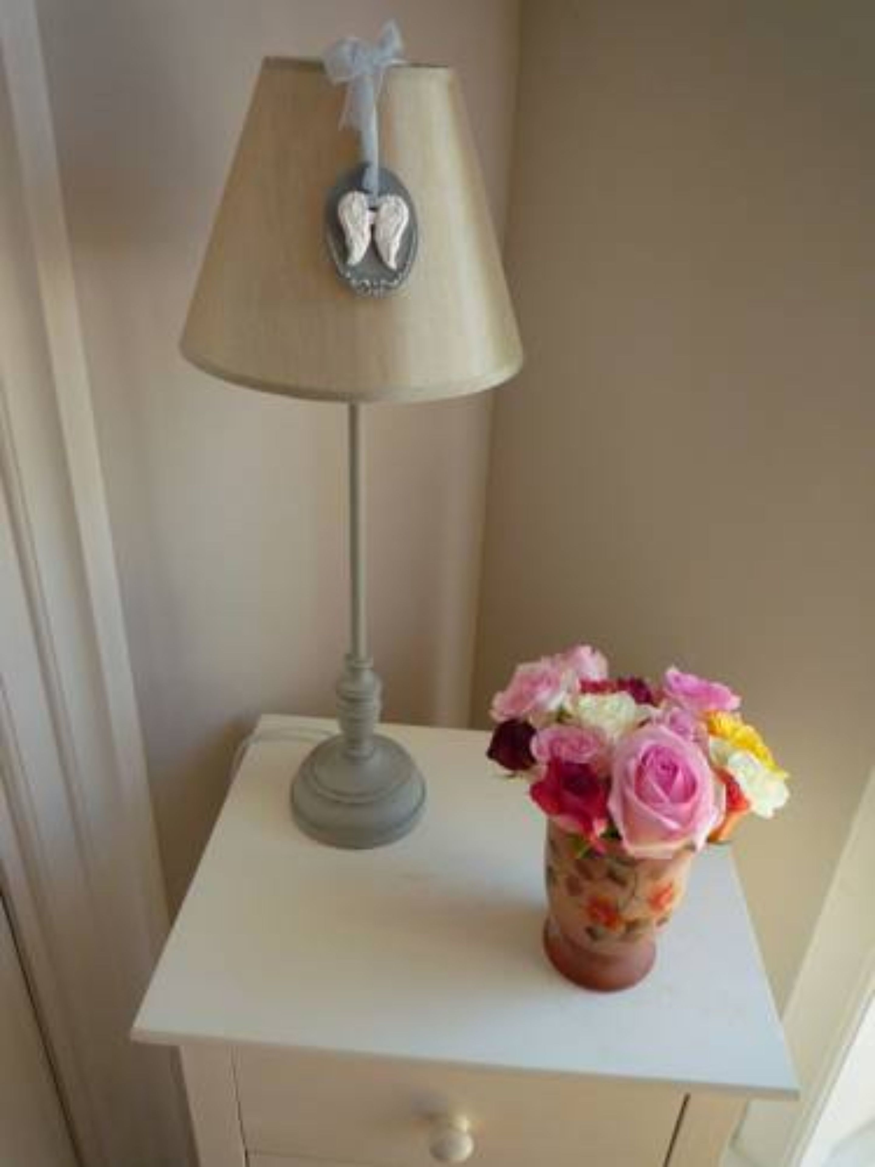 A bedside table with a lamp and a vase of flowers.