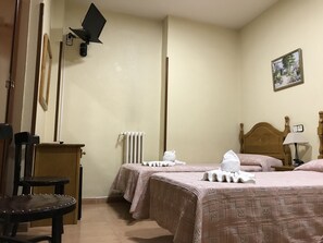 A hotel room with two beds, a wooden chair, a radiator, and a painting on the wall. - Hostal Internacional (Madrid)