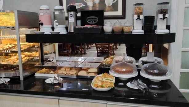A breakfast buffet counter with various food items, coffee machines, and a sign prohibiting food removal from the cafe. - Universitário Hotel (Itapetininga)
