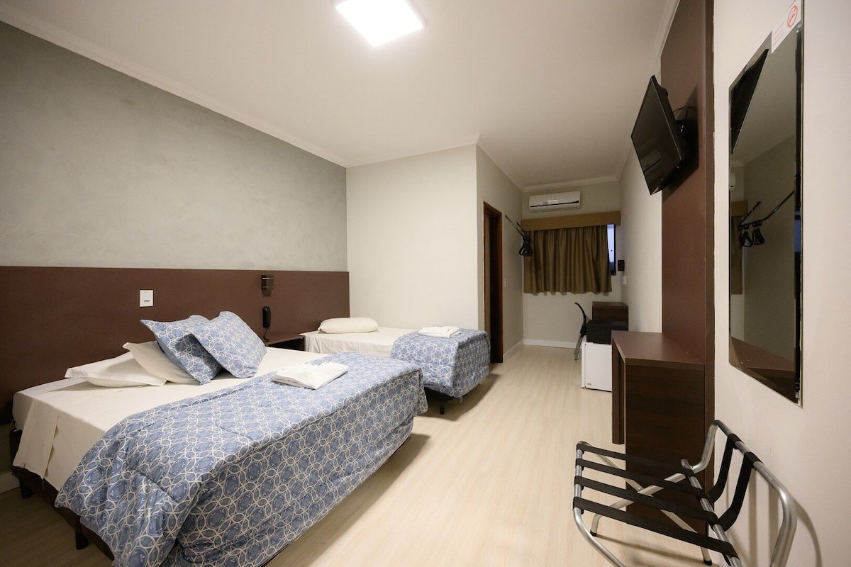 A hotel room with two beds, a desk, a chair, a TV, and an air conditioning unit.