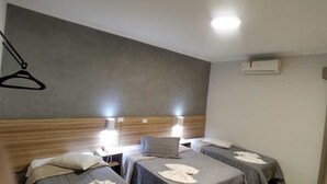 A hotel room with two single beds, a wooden headboard, bedside lamps, and a wall-mounted air conditioning unit. - Universitário Hotel (Itapetininga)