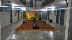 A spacious indoor area with a central garden, multiple doors, and a ceiling with exposed beams. - Universitário Hotel (Itapetininga)