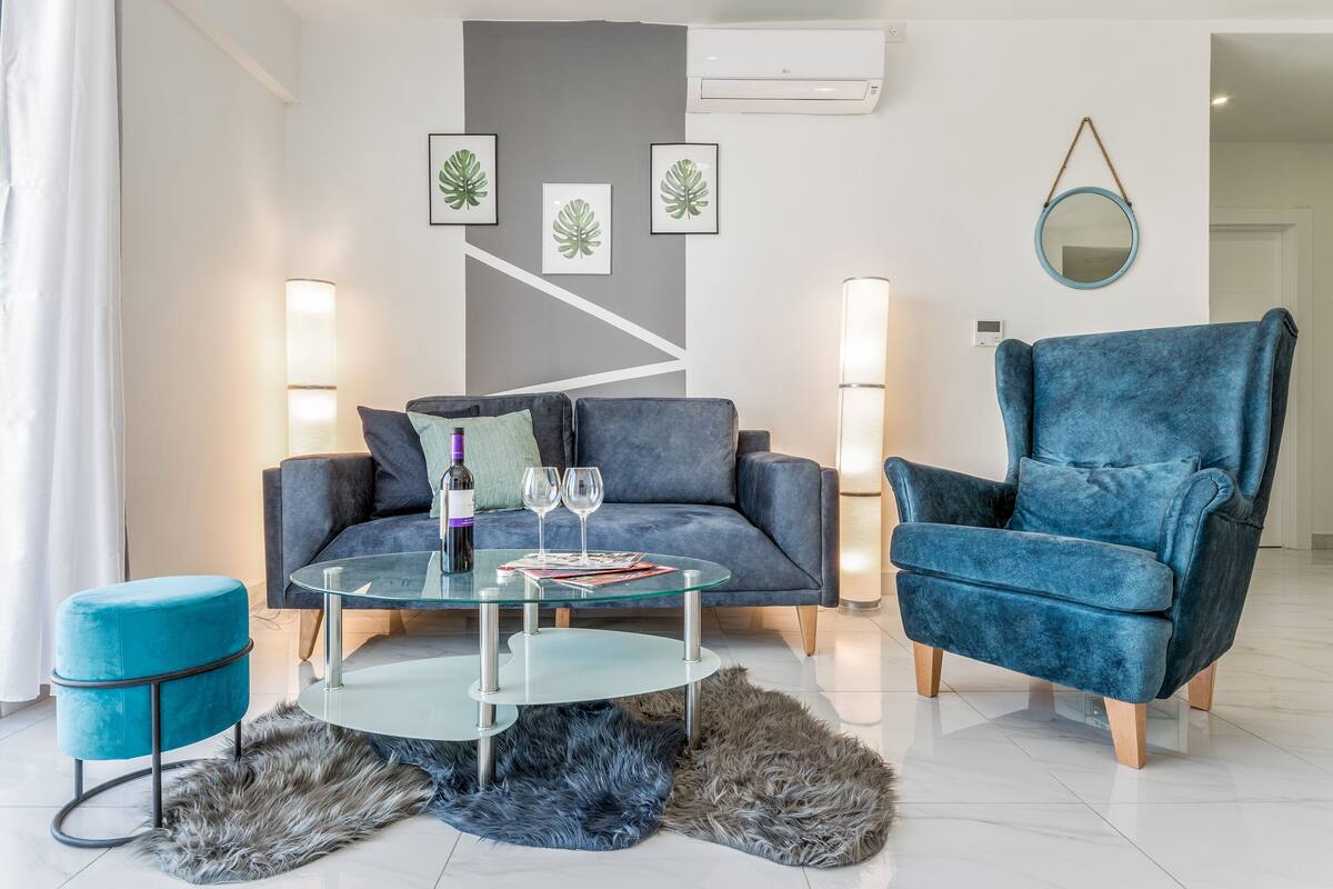 Ein modernes Wohnzimmer mit einer Couch, einem Sessel, einem Glastisch und einem kleinen Hocker.