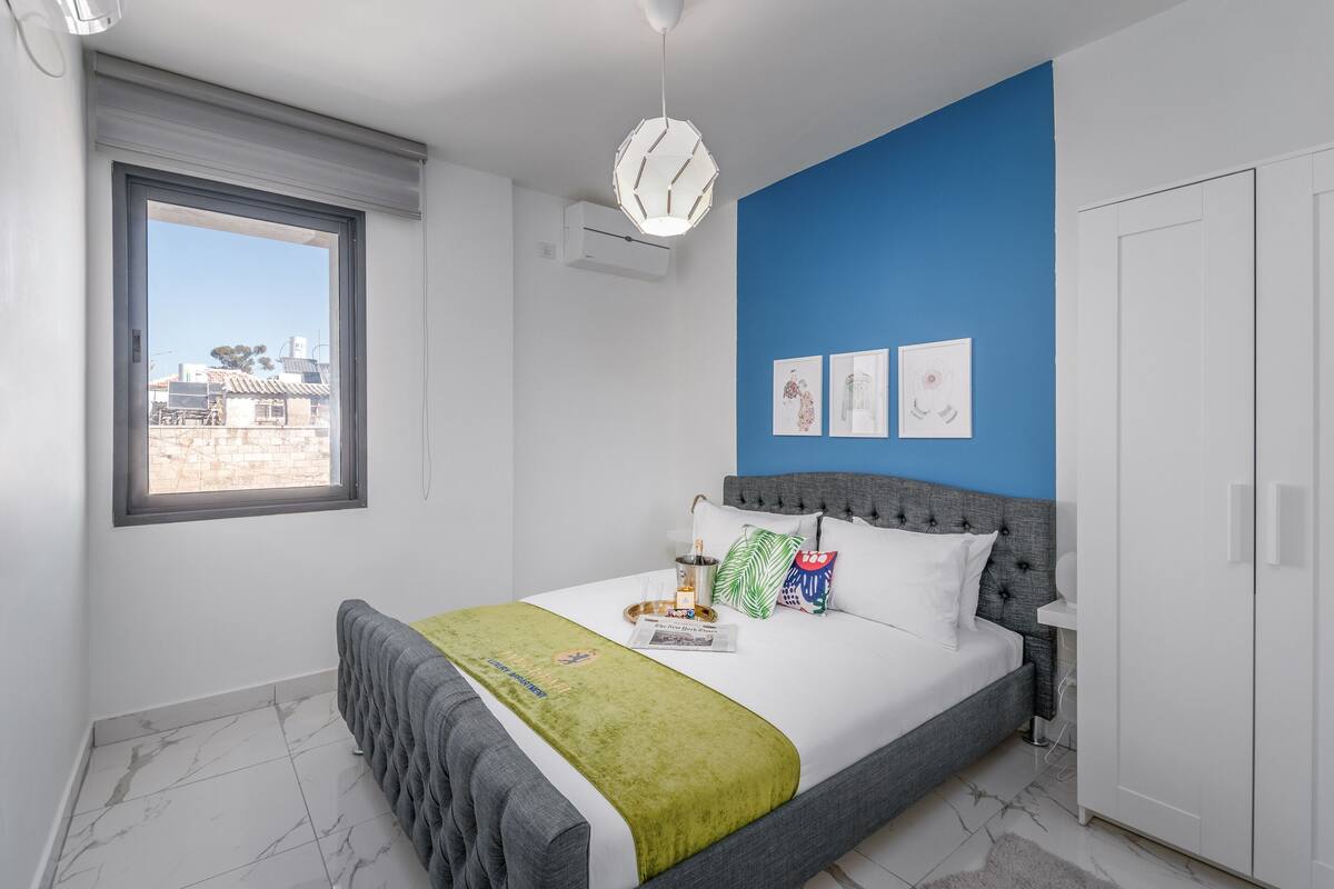 Ein Schlafzimmer mit einem Bett, einem Fenster, einer blauen Wand und einem weißen Kleiderschrank.