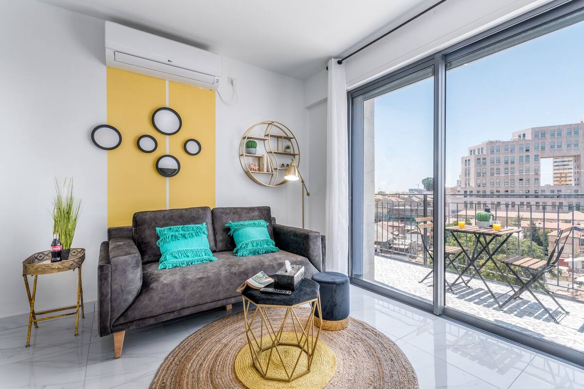 Ein modernes Wohnzimmer mit einem grauen Sofa, einem runden Couchtisch und einem großen Fenster mit Blick auf die Stadt.