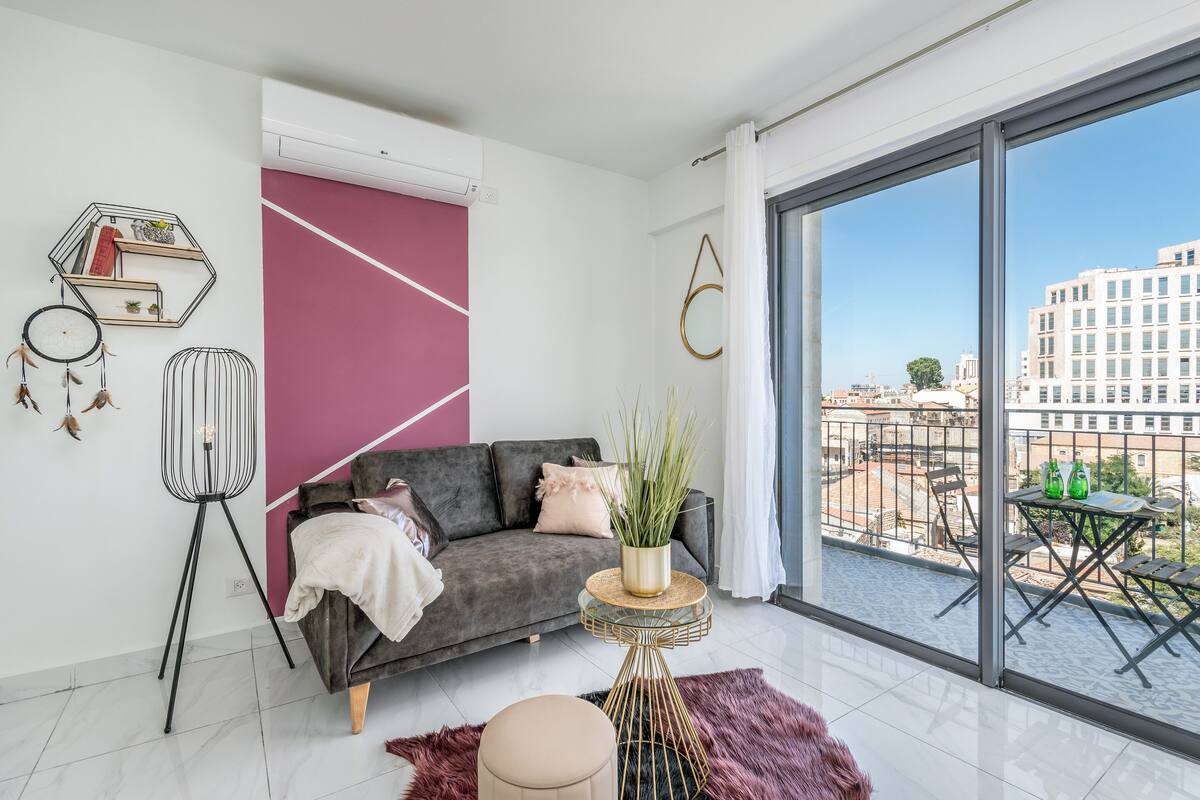 Ein modernes Wohnzimmer mit einem grauen Sofa, einem runden Couchtisch und einem großen Fenster mit Blick auf die Stadt.