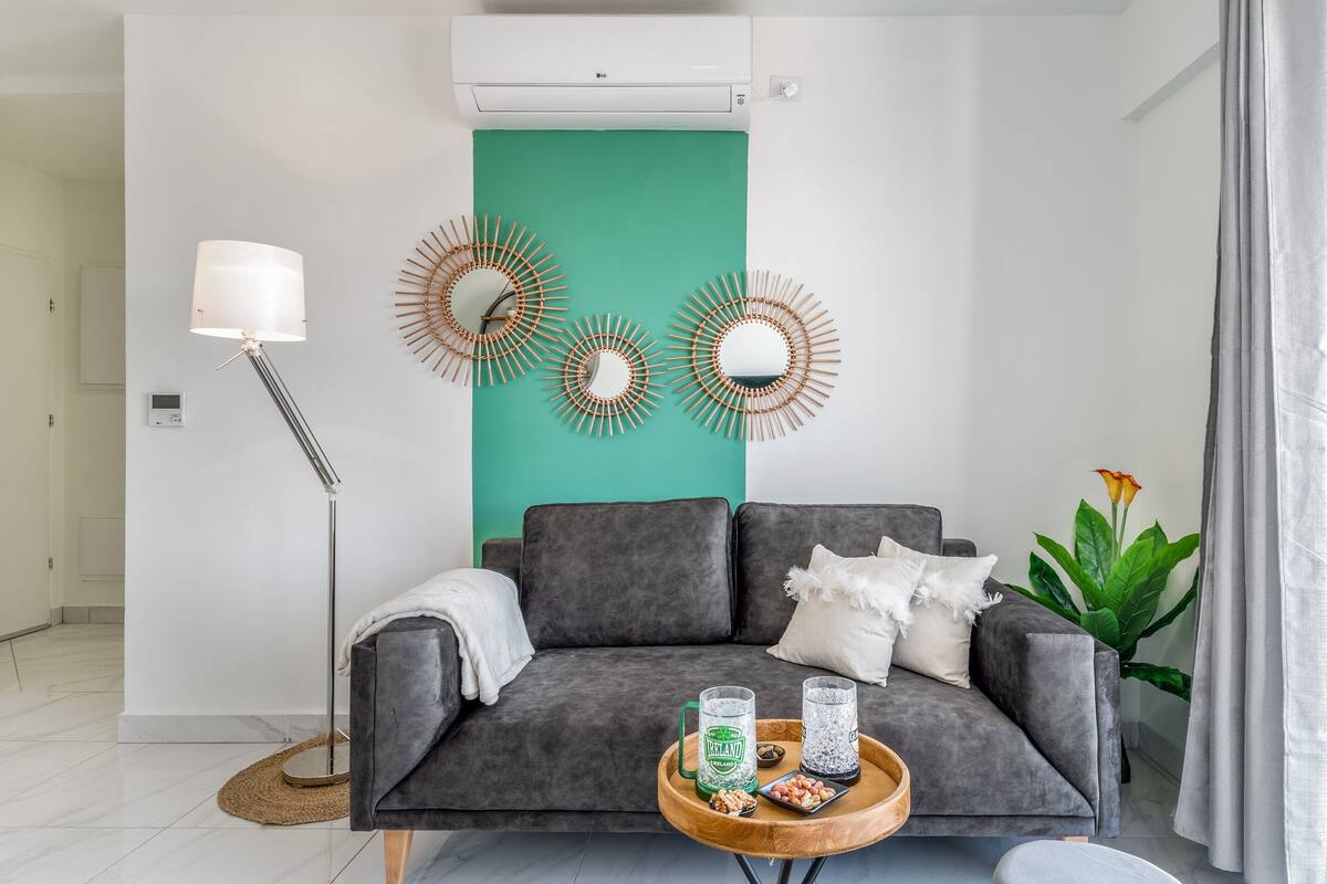Ein modernes Wohnzimmer mit einem grauen Sofa, einem Couchtisch mit Getränken, Wanddekoration und einer grünen Akzentwand.