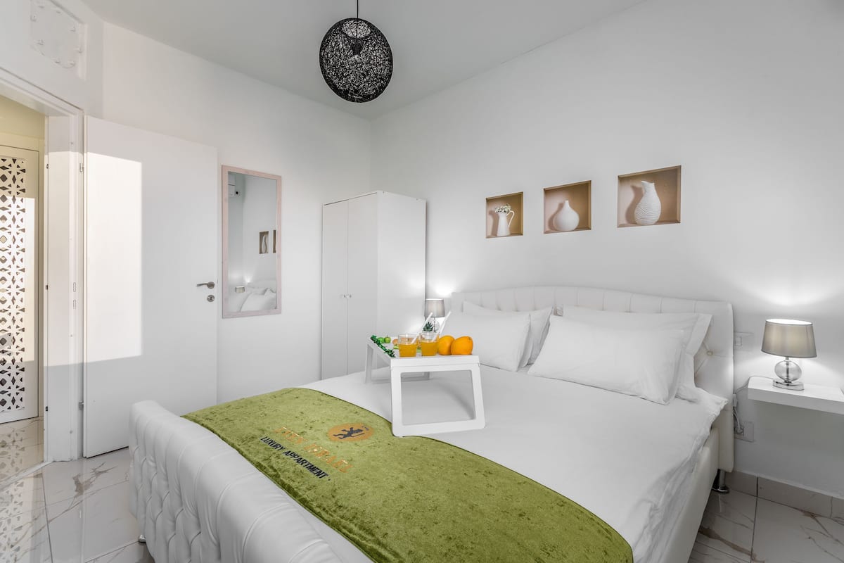 Ein modernes Schlafzimmer mit einem ordentlich bezogenen Bett, einem Nachttisch mit Lampe und einem kleinen Beistelltisch mit einer Vase.