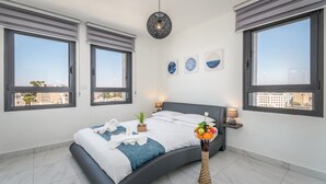 A modern bedroom with a curved bed, large windows, and a city view. - Even Israel Apartments (Jerusalem)