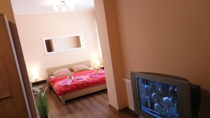 Un dormitorio con cama, televisor y una planta pequeña.