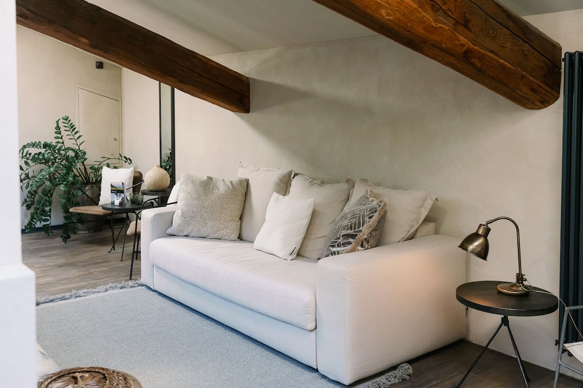 Uma sala de estar moderna com um sofá branco, uma mesinha redonda com abajur e uma planta grande.