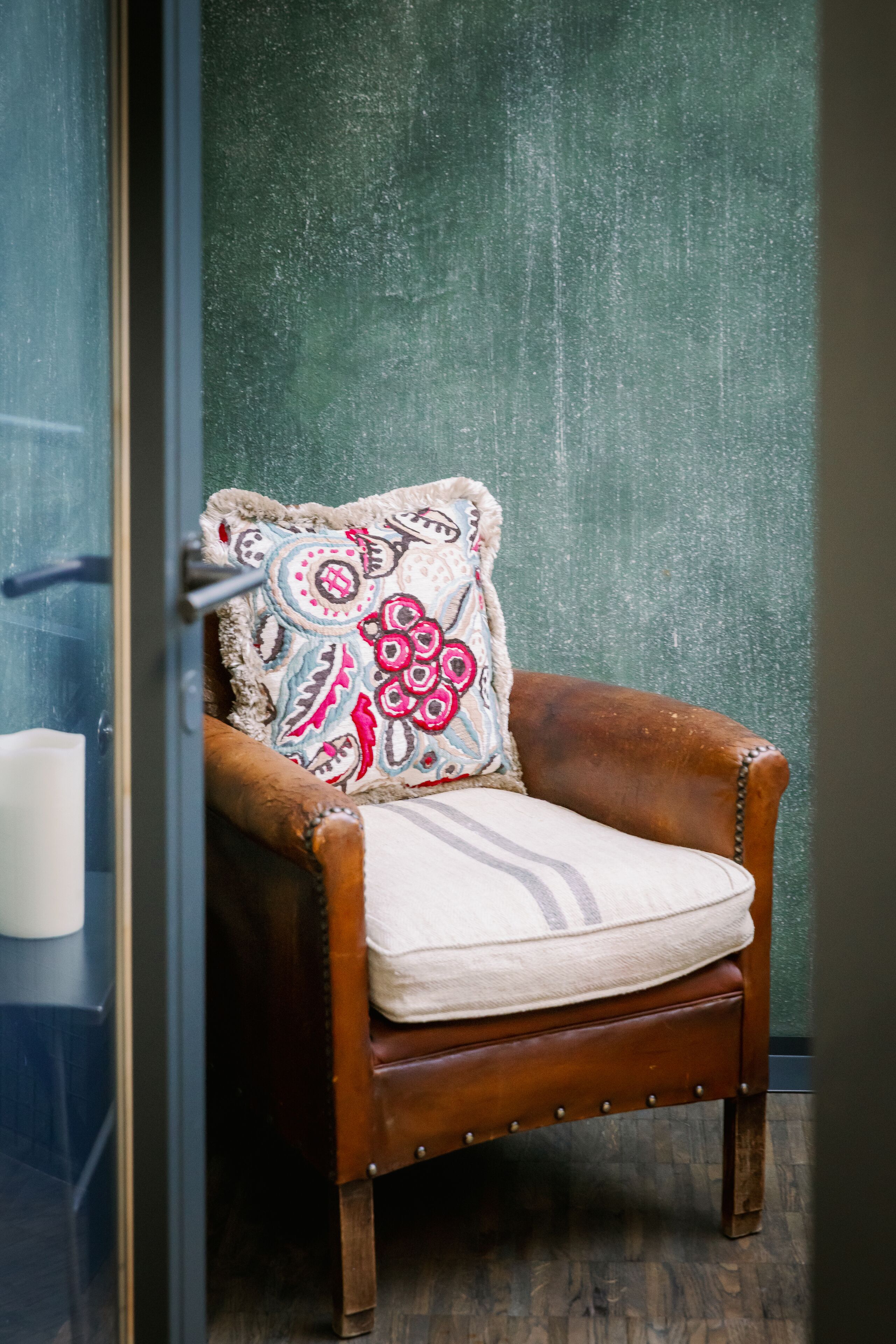 Un sillón de madera con un cojín estampado frente a una pared verde con textura.