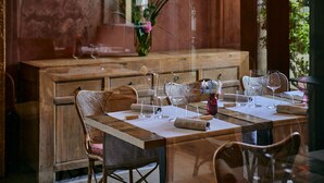 Un coin repas avec une table en bois dressée pour deux personnes, des chaises en osier et un vase rempli de fleurs.