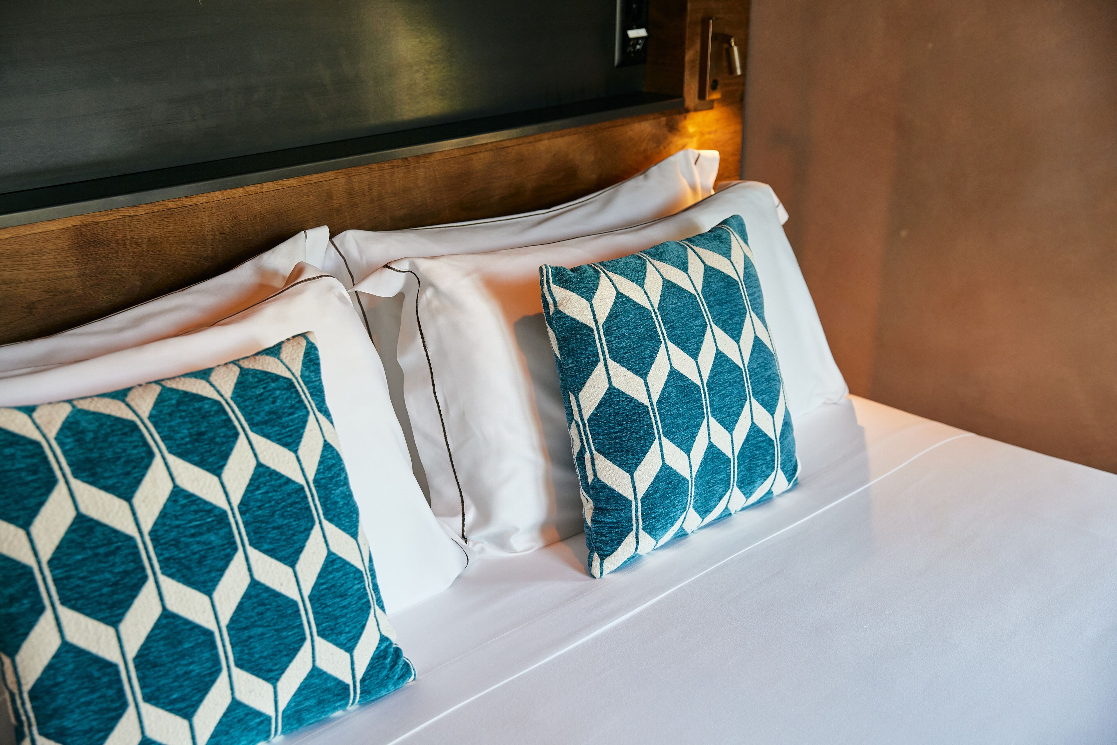 A neatly made bed with white linens and two patterned pillows.