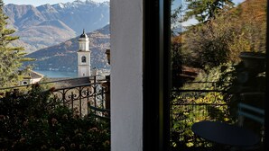 Une vue sur un paysage montagneux avec un clocher d’église, un lac et un balcon avec une table.