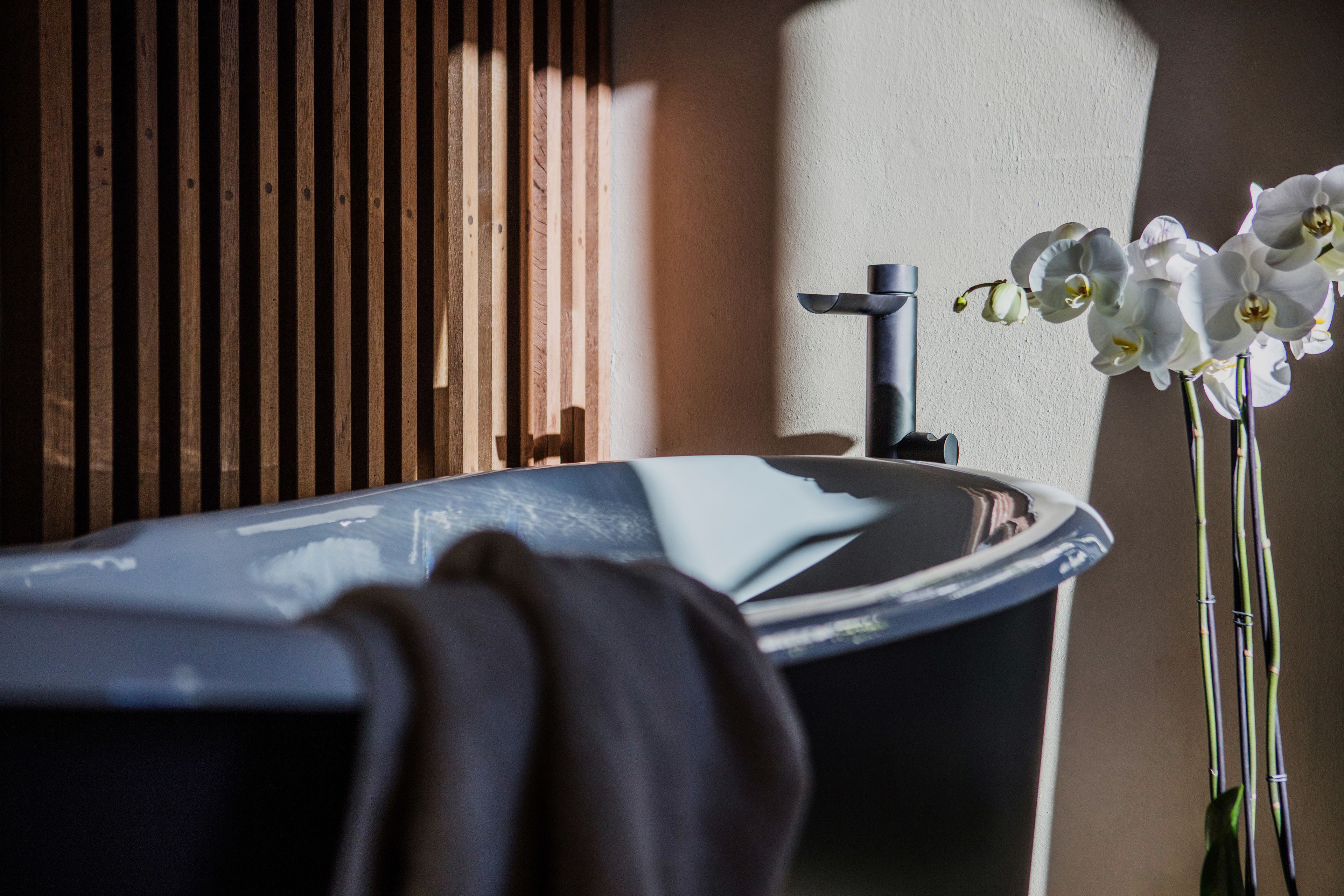 A bathroom with a bathtub, a towel, and white orchids.
